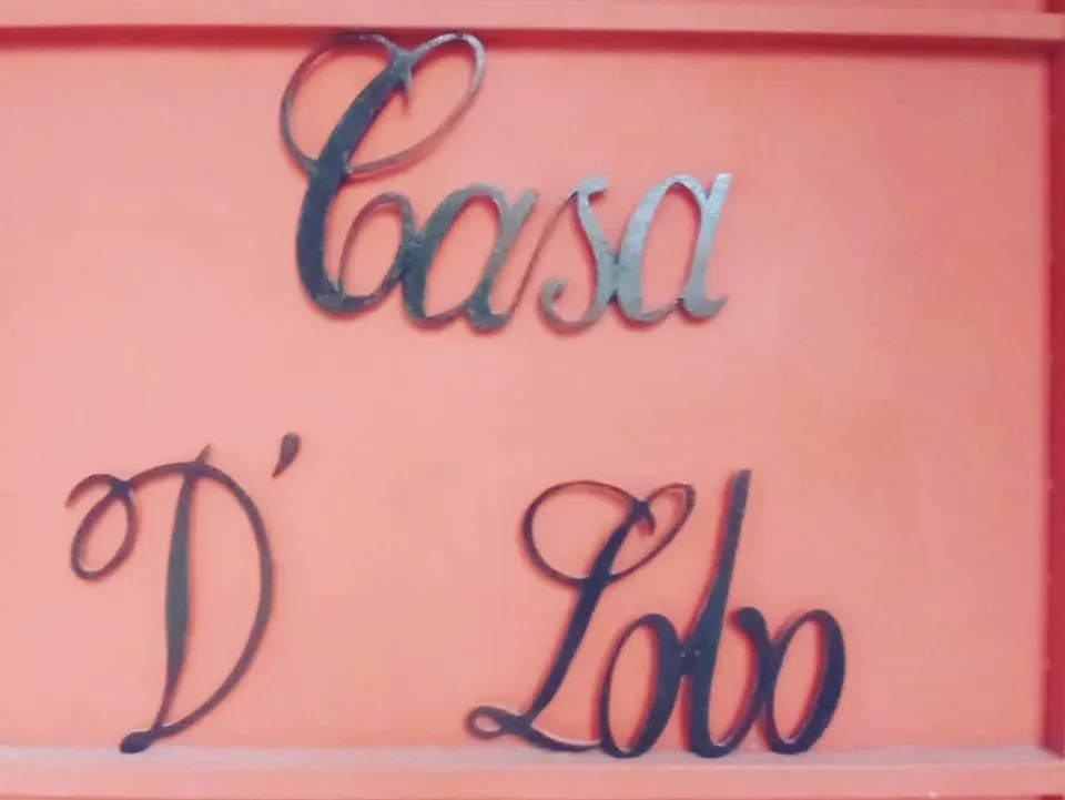 Letrero de herrería con el nombre Casa D'Lobo en cursiva sobre el muro terracota de la entrada