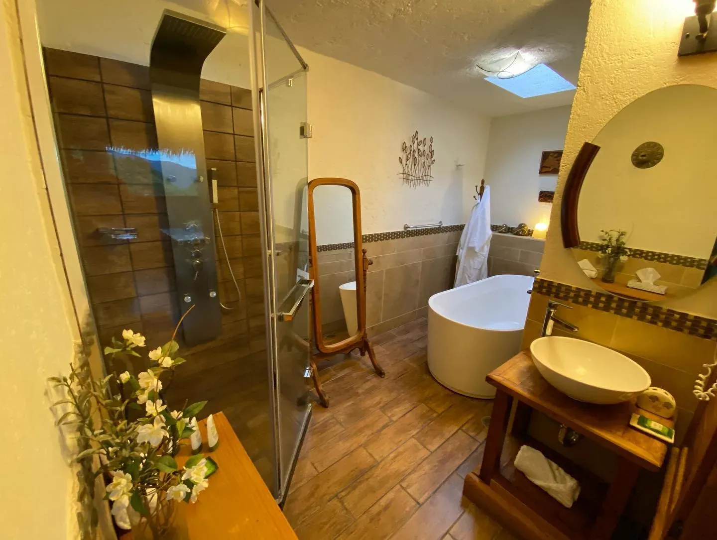 Baño de la Suite Principal visto desde la puerta: regadera de cristal, tina exenta y lavabo de piedra sobre mueble de madera