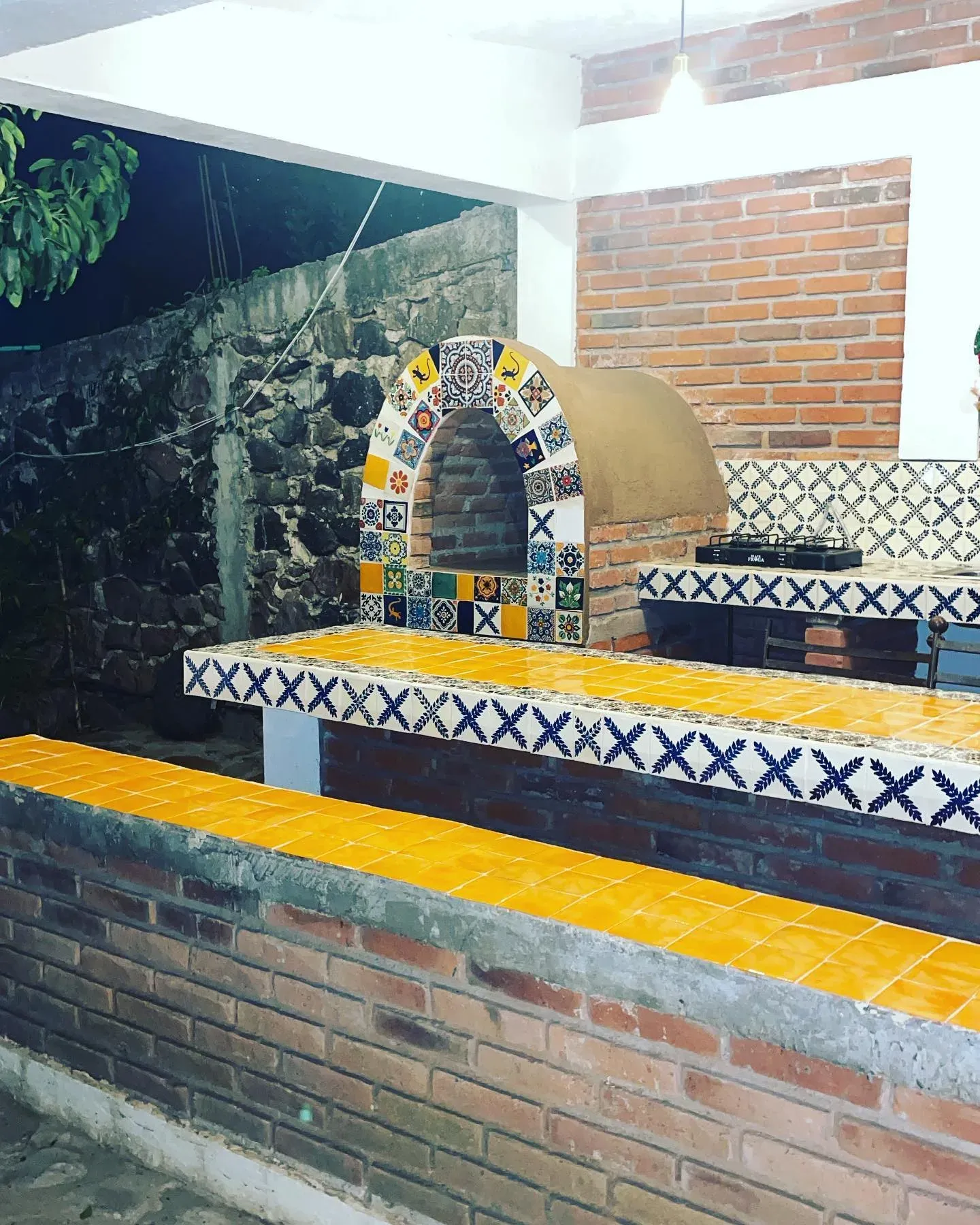 Horno de leña con arco de azulejo de talavera y barra de mosaico amarillo, contra un muro de ladrillo y piedra volcánica