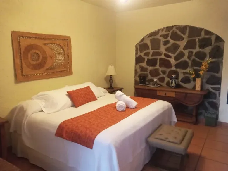 Habitación en planta baja con cama de camino naranja, nicho de piedra volcánica con consola y tapete tejido en el muro