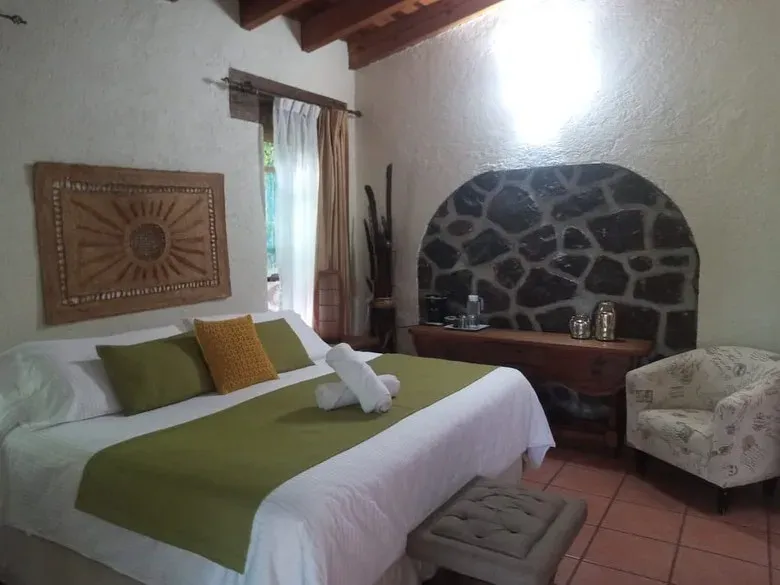 Habitación con vigas de madera, textiles verde olivo, nicho de piedra volcánica y sillón junto a la puerta a la terraza
