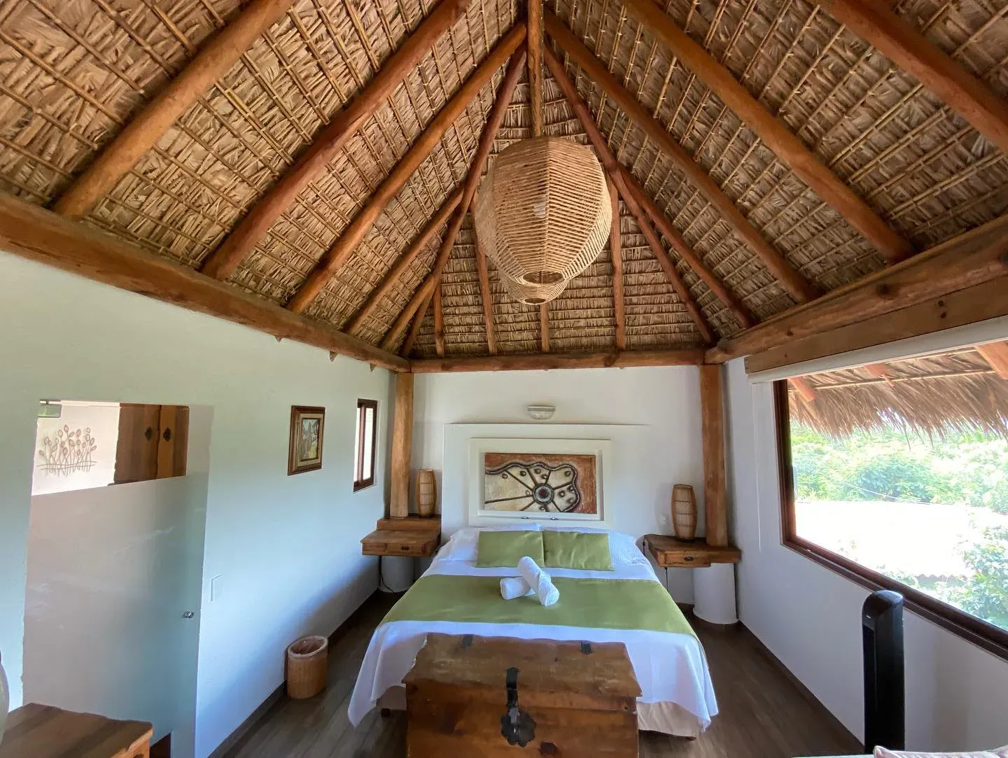 Interior amplio de la Suite Principal con techo de palapa a dos aguas, vigas de madera, cama king y ventanal al valle
