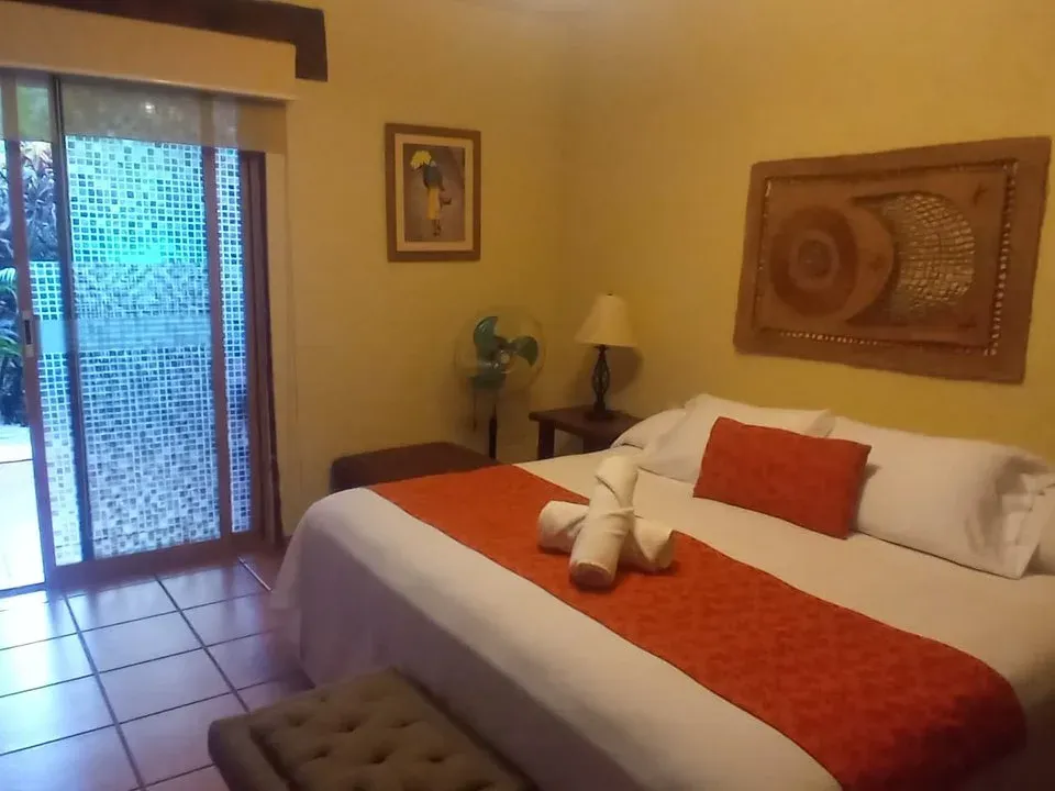 Habitación de muros ocre y piso de barro, con camino naranja sobre la cama y puerta corrediza al jardín interior